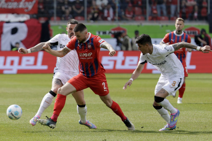 Marnon Busch de Heidenheim (C) reacciona ante el acoso de Aleix Garcia (i) y el ecuatoriano Piero Hincapie del Leverkusen (R) durante el cotejo de Bundesiga.