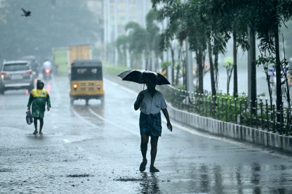 Un hombre que sostiene un paraguas viaja por una calle mientras llueve en Chenna.