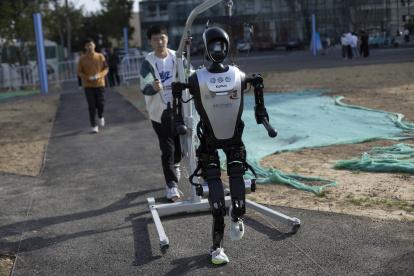 Un técnico camina detrás de un robot humanoide antes de la carrera de humanos y robots en Pekín.