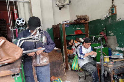 Oswaldo Cujilema (de pie) cose la planta de una zapatilla en su local “Cosedora Los Andes”, donde continúa el legado de su abuelo zapatero.