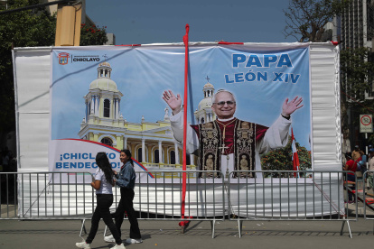 AME6509. LIMA (PERÚ), 10/05/2025.- Personas pasan frente a una pancarta con la imagen del papa León XIV este sábado, en la Plaza de Armas en Chiclayo (Péru). Rebosa la actividad en la plaza central de Chiclayo, localidad peruana donde el nuevo papa fue obispo ocho años y en la que los obreros ultiman las pantallas gigantes que retransmitirán una gran misa multitudinaria de acción de gracias de este sábado por la noche, mientras la Policía ultima las medidas de seguridad. EFE/ Paolo Aguilar