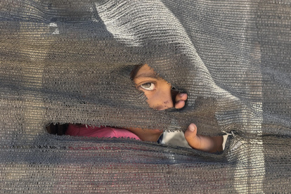 Una niña se asoma tras una tienda improvisada en el puerto en la Ciudad de Gaza, donde miles de personas desplazadas por los ataques israelíes han encontrado refugio, el 20 de mayo de 2025.
