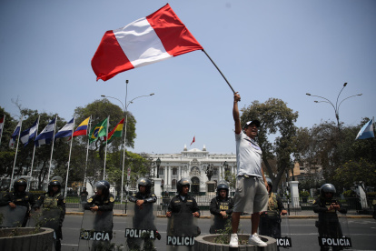 Fotografía de un hombre al ondear una bandera peruana, frente a la sede del Congreso Nacional de Perú, en Lima (Perú).