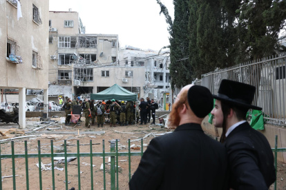Dos hombres judíos ultraortodoxos cerca de una escuela de niñas judías dañada después de que misiles balísticos iraníes impactaran Bnei Brak, en el centro de Israel, el 16 de junio de 2025.