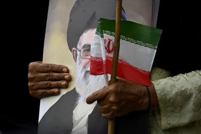 Un musulmán chiita pakistaní sostiene un retrato del líder supremo de Irán, Alí ​​Jamenei, y una bandera nacional de Irán durante una manifestación en solidaridad