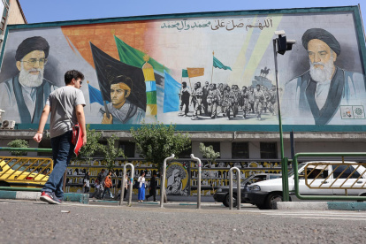 Iraníes caminan junto a una pintura mural del líder supremo iraní, el ayatolá Ali Jameneí (arriba-i) y el fallecido líder supremo iraní, el ayatolá Ruhollah Jomeiní (arriba-d), en una calle de Teherán.