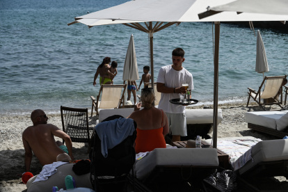A waiter serves drinks to sunbathers sitting on their sunbeds along the beach on the Halkidiki Peninsula, northern Greece on June 13, 2025. After a year in which a record number of international tourist arrivals were recorded in Greece, more than 36 million people, and optimistic forecasts for 2025, thousands of jobs in tourism businesses remain vacant at the start of the tourist season. (Photo by Sakis Mitrolidis / AFP)
Personal. Un camarero sirve bebidas a los bañistas sentados en sus tumbonas a lo largo de la playa en la península de Halkidiki, en el norte de Grecia, en junio de 2025.