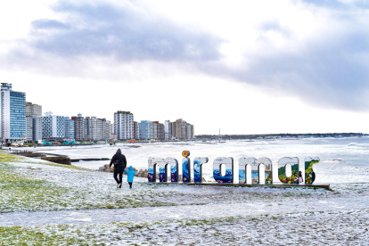 Personas caminan en una playa cubierta de nieve este lunes 30 de junio de 2025, en Miramar (Argentina).