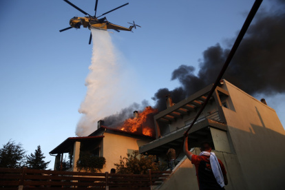 Un helicóptero de bomberos y voluntarios luchan para apagar un incendio que quema casas en la zona residencial de Kryoneri, en las afueras de Atenas, Grecia, este sábado 26 de julio.