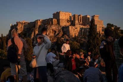 Los turistas disfrutan de una puesta de sol mientras están sentados en la colina del Areópago con vistas a la antigua Acrópolis de Atenas.