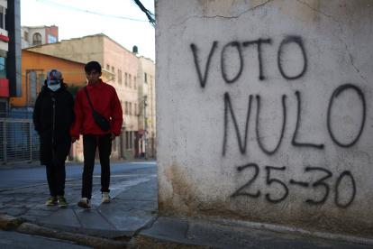 Personas caminan junto a un mural con un mensaje alusivo a la elecciones este sábado, en La Paz (Bolivia).