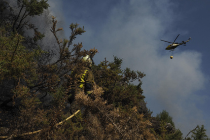 Un helicóptero de la lucha contra el fuego vuela sobre un bombero que trabaja en la extinción del incendio.(Lugo, Galicia).