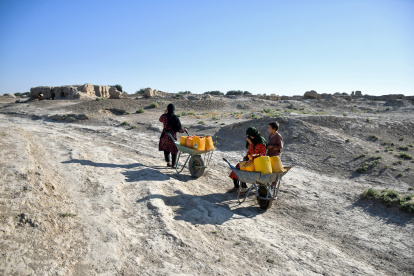 Carencia. Una mujer afgana con sus hijos toma un descanso mientras transportan bidones de agua en carretillas en el pueblo de Bolak.