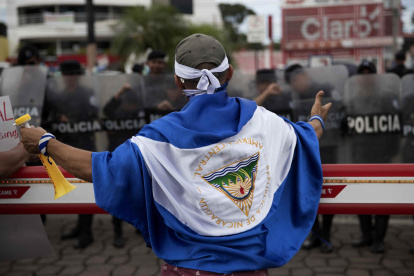 Joven con una bandera de Nicaragua frente a Policías, en Managua (Nicaragua).