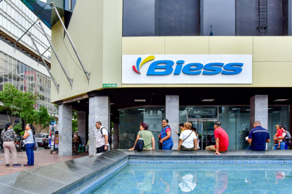 Usuarios del Banco del Instituto Ecuatoriano de Seguridad Social (Biess) y ciudadanía en general se sientan en el borde de una pileta ante la escasez de espacios adecuados.