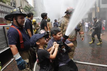 NIÑOS SOSTIENEN LA MANGERA DE BOMBERO. Ejercicio de agua q ue se lleva a cabo en la Avenida 9 de Octubre por parte de los bomberos, en homenaje a las fiestas de la ciudad / Jimmy Negrete Vera / Expreso / Guayaquil-Ecuador / 04 Octubre 2015 / Ag-Expreso.