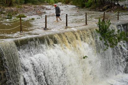 Un hombre cruza un badén inundable durante este lunes en el que el aviso rojo (riesgo extremo). España.