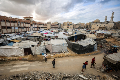 Un hombre y niños caminan junto a tiendas de campaña que albergan a personas desplazadas por la guerra, instaladas cerca de la mezquita Sheikh Hamad bin Khalifa Al-Thani, gravemente dañada.