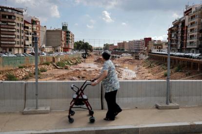 Restos. Una adulta mayor camina sobre un puente mientras trabajadores instalan estructuras y enormes piedras en el seco canal artificial de Paiporta.