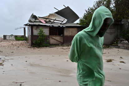 Una persona camina frente a una casa afectada por los vientos preliminares del huracán Melissa, en la playa pesquera de Hellshire, en Portmore (Jamaica).