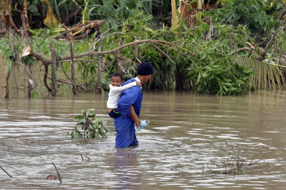 Fotografía del 29 de octubre de 2025 de un hombre cruzando un río crecido mientras carga a un niño, en el poblado de Guama en Santiago de Cuba (Cuba).