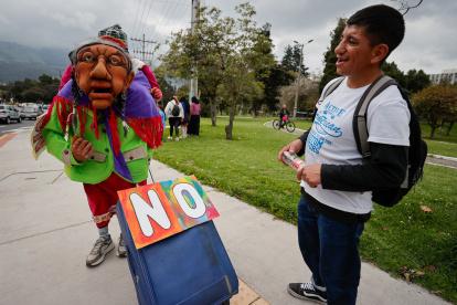 Una persona disfrazada sostiene una maleta mientras un hombre lo observa durante una manifestación contra el referéndum en Quito (Ecuador).