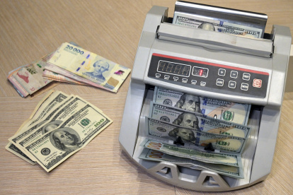 Una ilustración muestra una máquina contando billetes de pesos argentinos junto a billetes de dólares estadounidenses en Buenos Aires el 22 de octubre de 2025.