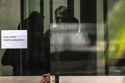 Bolsonaro aparece tras una puerta en la Policía Federal de Brasilia, donde explicó que quemó su tobillera electrónica tras sufrir “paranoia” por medicamentos.