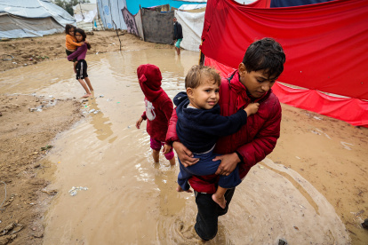 Niños palestinos caminan entre aguas inundadas tras fuertes lluvias en un campamento.