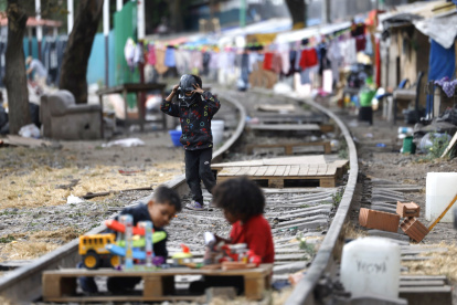 Hecho. Menores migrantes juegan sobre la vía de un campamento, en Ciudad de México (México), entre muros de madera, lonas y otros materiales reciclados.