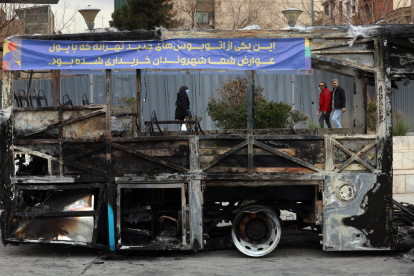 Iraníes caminan cerca de los restos de un autobús público incendiado en Teherán, Irán, el 15 de enero de 2026.