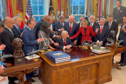 Donald Trump aparece sentado detrás de su escritorio, mientras un grupo de pastores evangélicos coloca sus manos sobre él y eleva una oración.