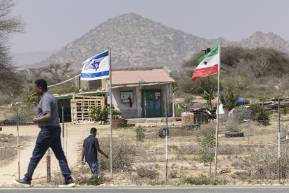 La gente camina junto a las banderas de Israel y Somalilandia que ondean juntas en la entrada de una granja de frutas.