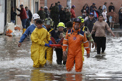 Integrantes de organismos de rescate socorren a un hombre en una calle inundada por fuertes lluvias este jueves, en Facatativá (Colombia).