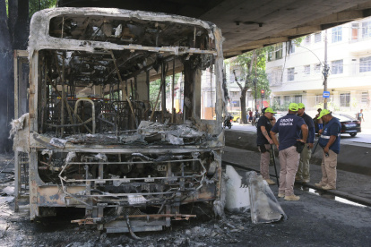 Bomberos observan los restos de un autobús incendiado por supuestos integrantes de una facción criminal, en respuesta a la muerte de Claudio Augusto dos Santos en Río de Janeiro