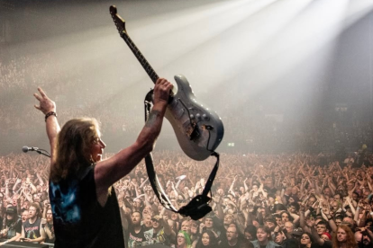 Integrante de Iron Maiden levanta su guitarra ante miles de fanáticos durante un concierto, en una escena que refleja la energía de la banda británica en vivo.
