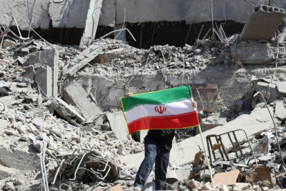 “Un ciudadano sostiene la bandera de Irán en medio de los escombros tras recientes ataques.