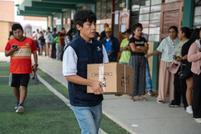 Integrante de la Oficina Nacional de Procesos Electorales (ONPE) carga una caja para empezar la instalación de una de las mesas de votación en un colegio de Lima.