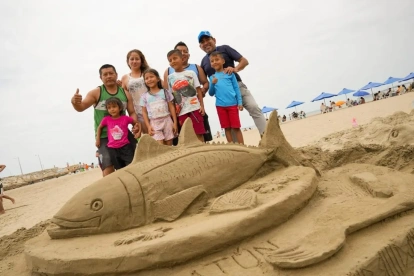 Un grupo de turistas se toma una foto frente a una escultura hecha con arena en una playa de Manabí.