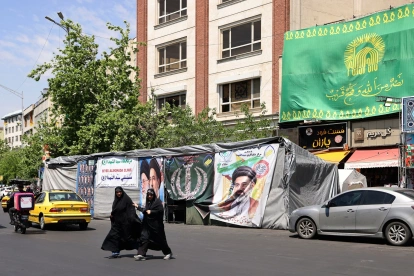 Mujeres caminan junto a pancartas instaladas a lo largo de la carretera con imágenes del asesinado líder supremo de Irán, el ayatolá Ali Khamenei (izquierda), y del líder supremo, el ayatolá Mojtaba Khamenei, en Teherán.