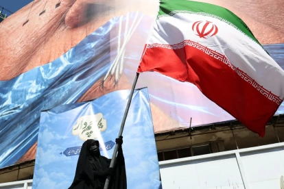 Una mujer con velo sostiene la bandera nacional de Irán frente a una enorme valla publicitaria antiestadounidense en Teherán, Irán, el 11 de mayo de 2026.