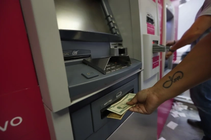 Personas usan los cajeros automáicos para retirar o depositar dinero.