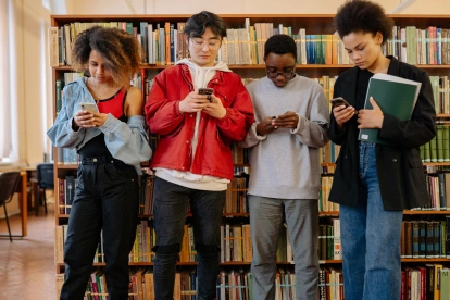 Estudiantes consultan sus teléfonos en una biblioteca, mientras Noruega restringe el uso de inteligencia artificial para menores de 6 a 13 años.
