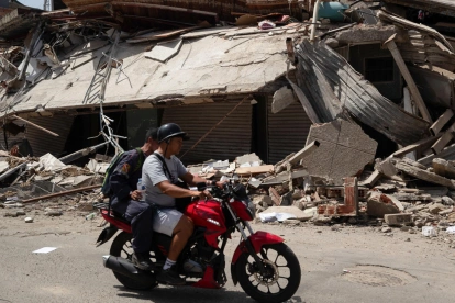 Personas transitan en motocicleta frente a edificios colapsados por los terremotos en Catia La Mar, Venezuela.