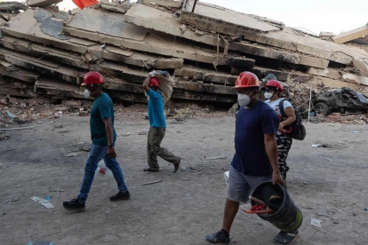 Personas caminan frente a los escombros de un edificio tras los sismos en La Guaira, Venezuela.