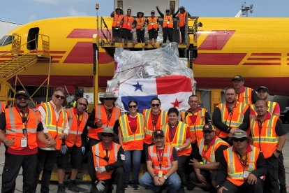 Personal de carga junto a un envío con la bandera de Panamá en un avión de DHL