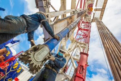 Dos personas hacen labor de mantenimiento en una torre donde se extrae petróleo.