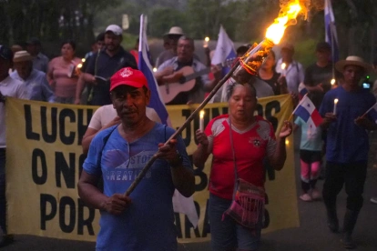 Campesinos sostienen banderas y velas en una vigilia en rechazo al decreto ejecutivo que ordena la clausura de los cementerios comunitarios.