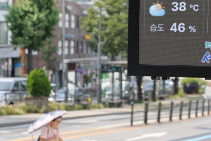 Un tablero digital muestra 38 °C en una calle de Pyongyang, mientras un transeúnte se protege del sol con sombrilla en plena ola de calor.
