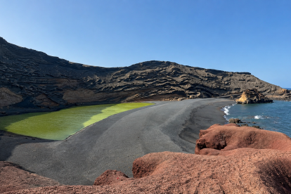 El Charco de los Clicos sorprende por sus aguas verdes rodeadas de arena negra, rocas rojizas y el azul del océano.